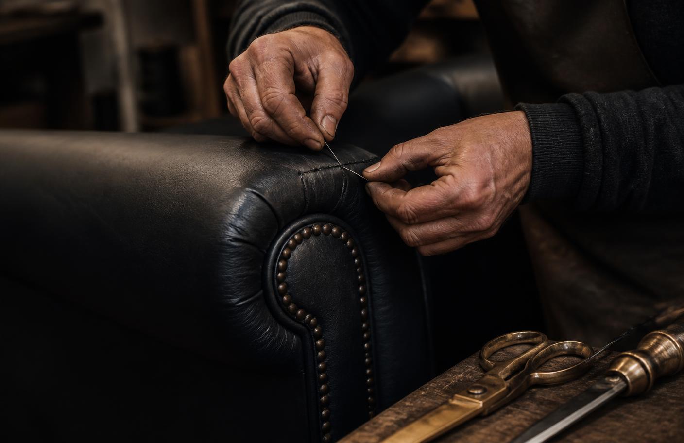 Craftsman hand-stitching the arm of a leather sofa